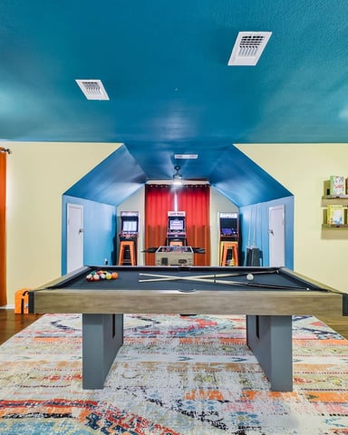 Colorful recreation room with pool table, arcade games, orange bar stools, and turquoise ceiling